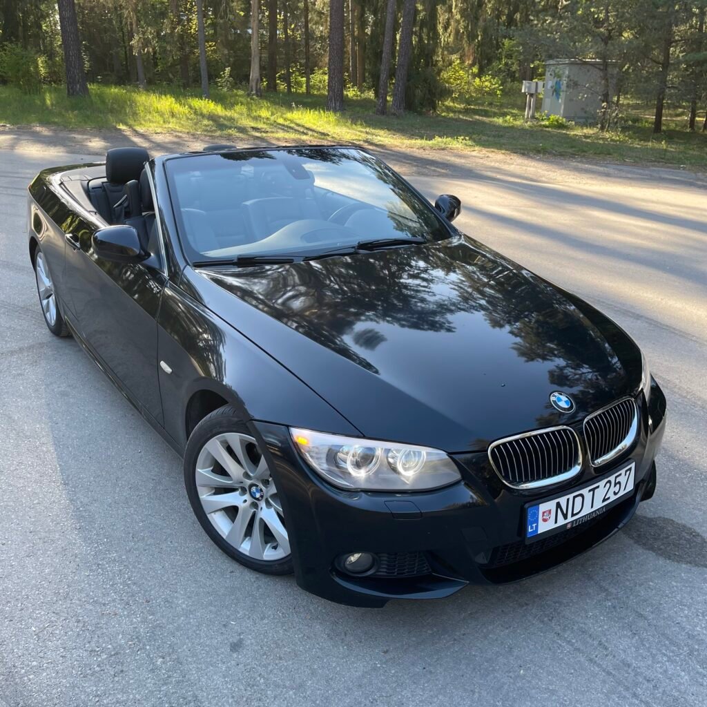 Juodas BMW 3 serijos kabrioletas (E93) nuleistu stogu saulėtą dieną miške – premium klasės BMW automobilių supirkimas brangiai visoje Lietuvoje.
